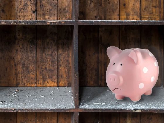A sad piggy bank sitting on a dusty shelf.