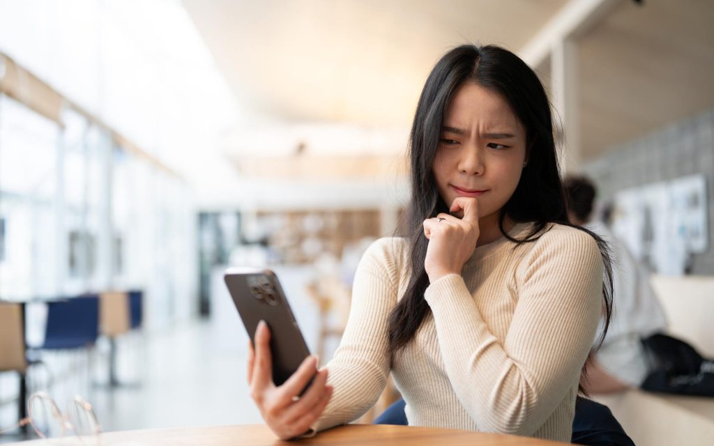 A woman looks suspiciously at her phone screen.